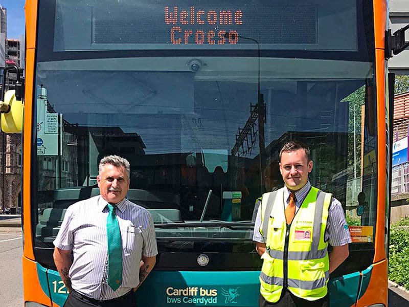 Two staff of Cardiff Bus standing in front of a vehicle.